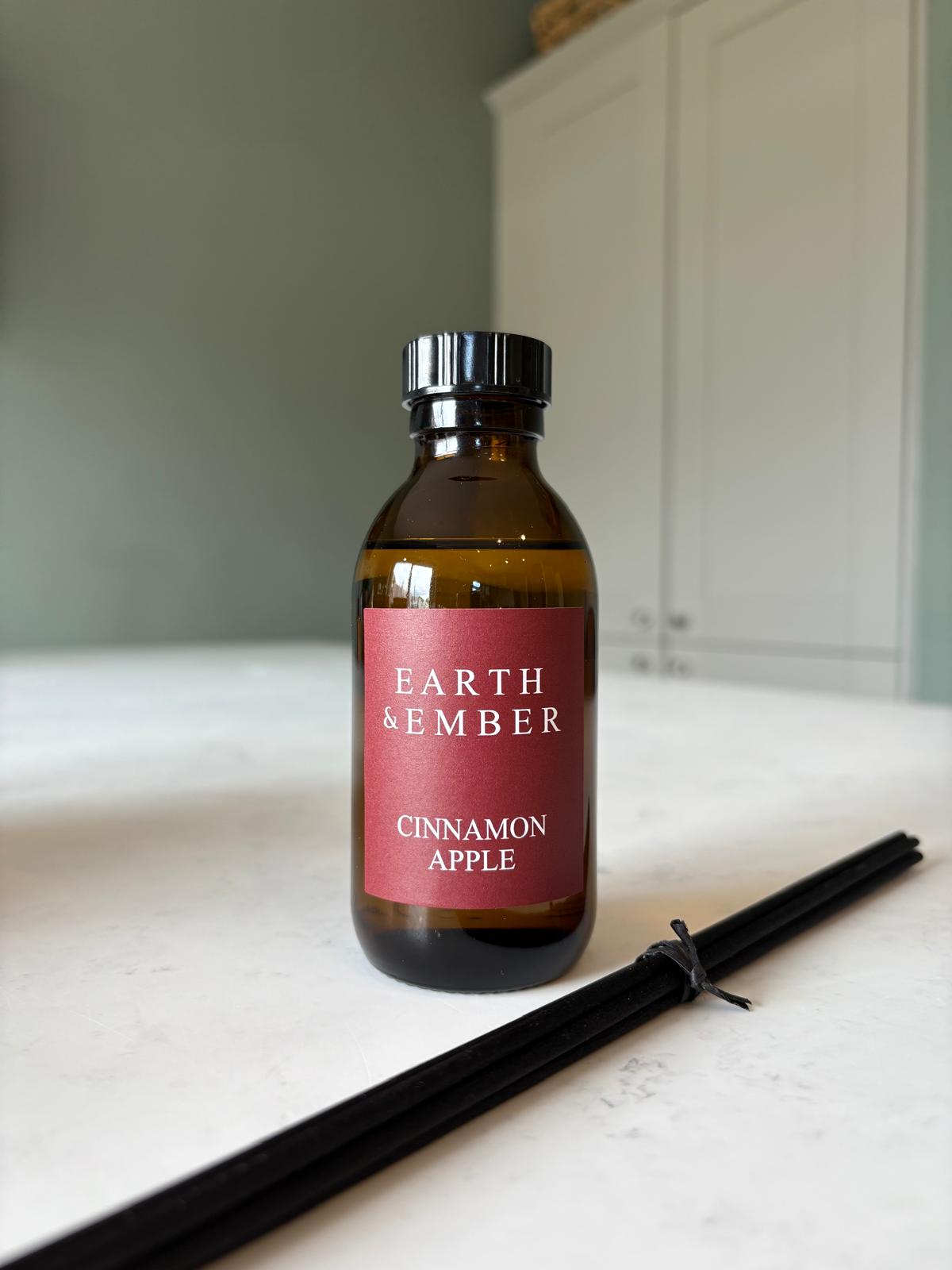 Bottle of 'Earth & Ember Cinnamon Apple' reed diffuser on a white surface with a neutral background. Autumn scent