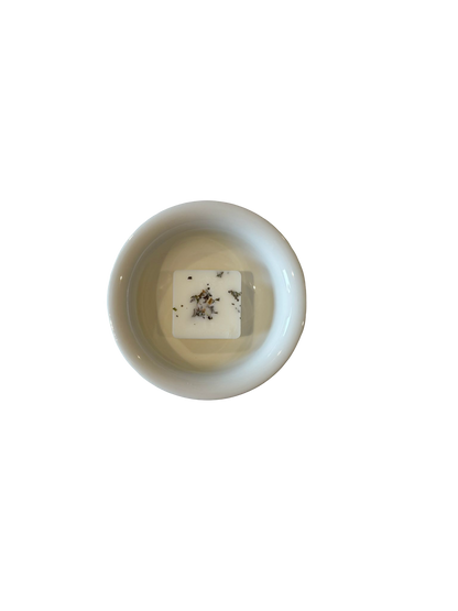 Small white dish with a square white soy wax melt candle inside on a light beige background
